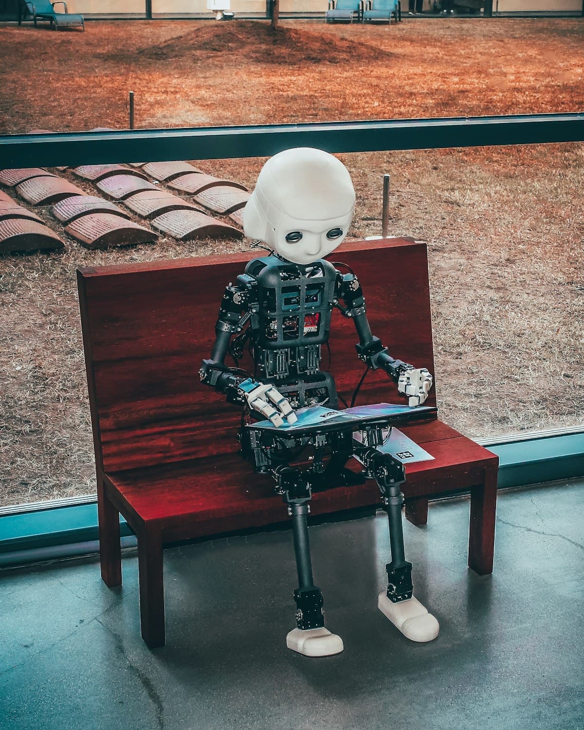 Small humanoid robot sitting on a red bench and using a tablet